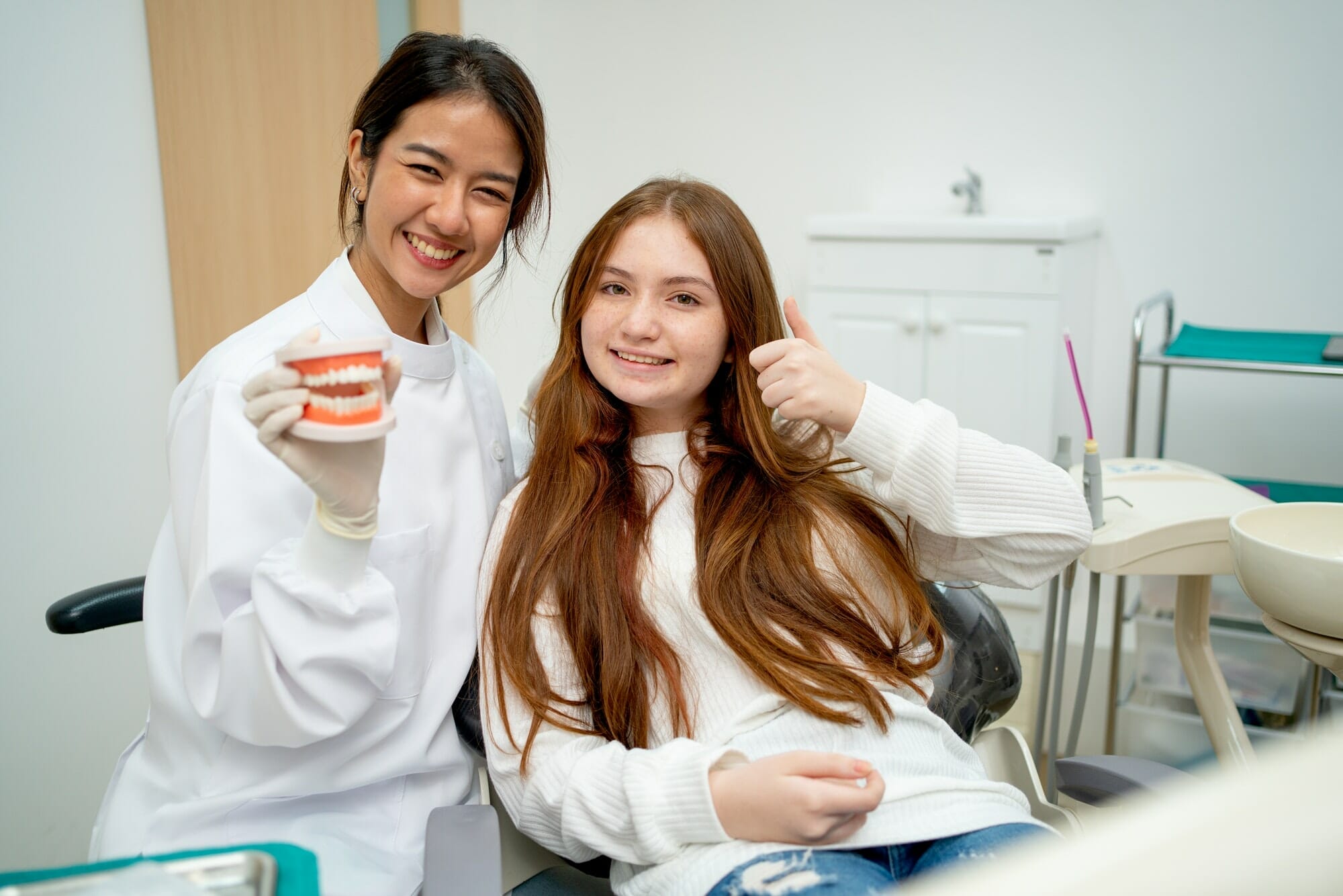 Asian cosmetic dentist stand with young girl and smile to camera also hold teeth model
